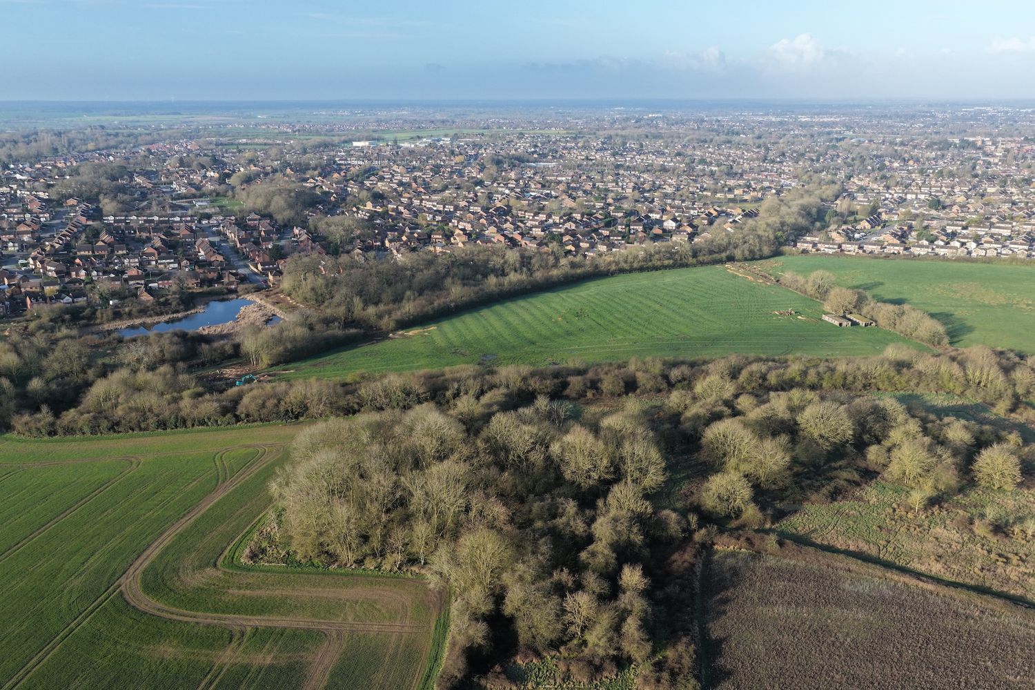 Aerial panoramic view of suburban neighborhoods and farmland showing residential development patterns along rolling hills.