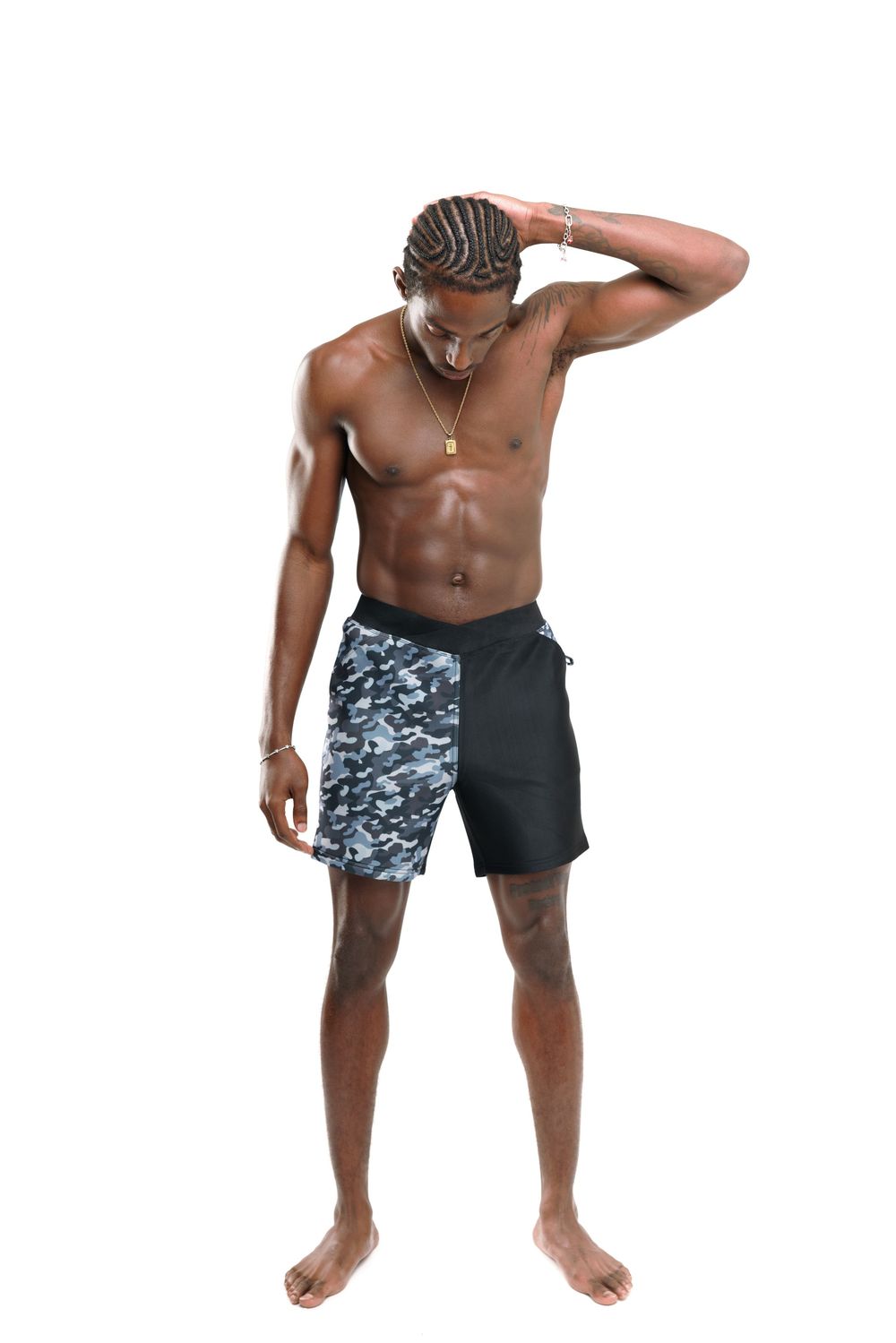 Athletic shirtless man wearing black and gray camo print shorts poses with hand on head against white background.