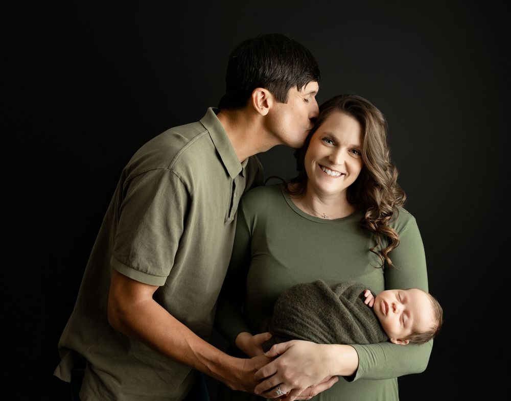 Dad kisses Mom while she holds the newborn. - Greenville, SC newborn photographer - Easley, SC newborn photographer.