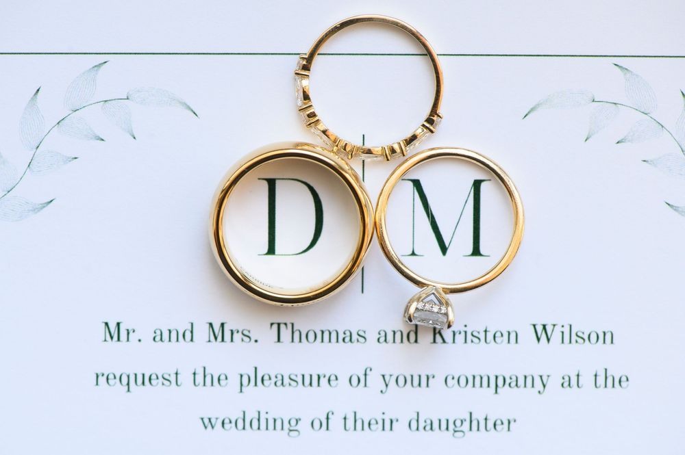 Gold wedding rings resting on elegant wedding invitation with initials D and M for Wilson family celebration.