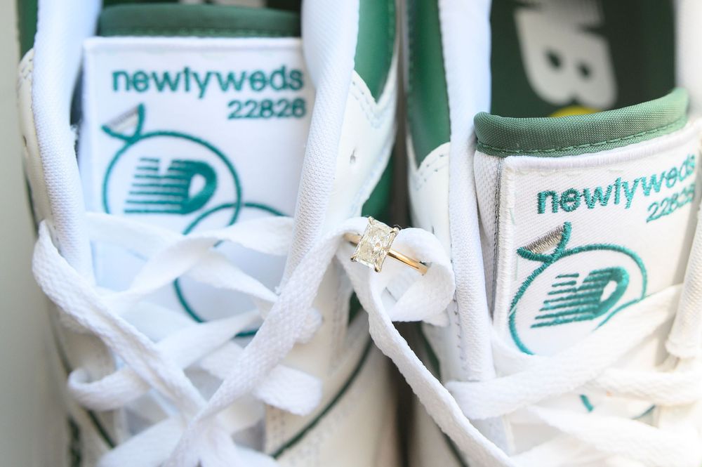 Custom New Balance sneakers reading 'newlyweds 22826' with a diamond ring resting on white laces.