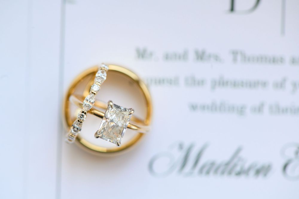 Gold wedding ring set with radiant cut diamond engagement ring and diamond band on wedding invitation.