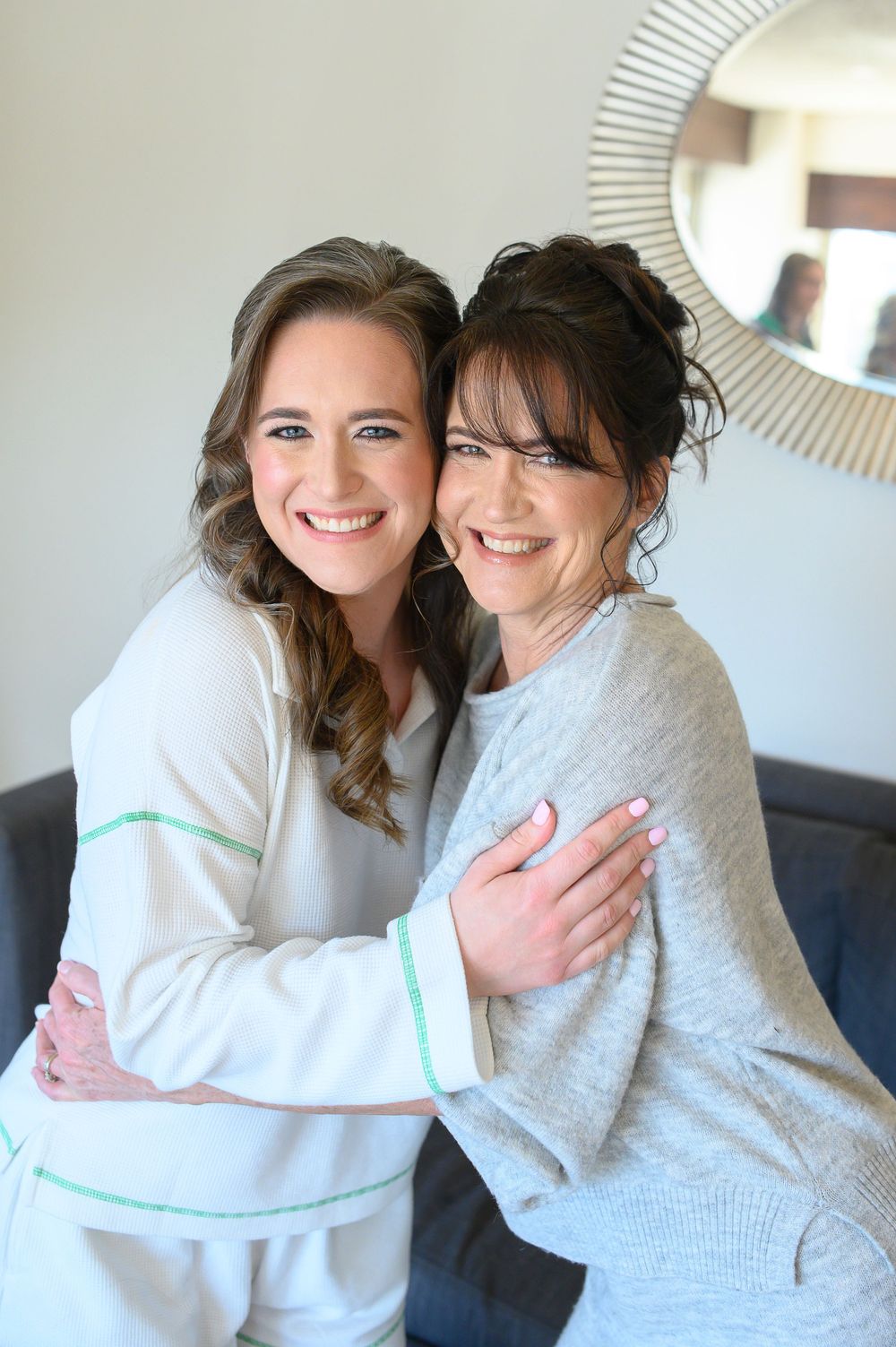 Two women smiling and embracing warmly, dressed in casual attire, posing together in a bright, elegant room.