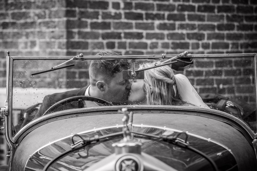 Black and white photo of bride and groom sharing a kiss in a vintage classic car.