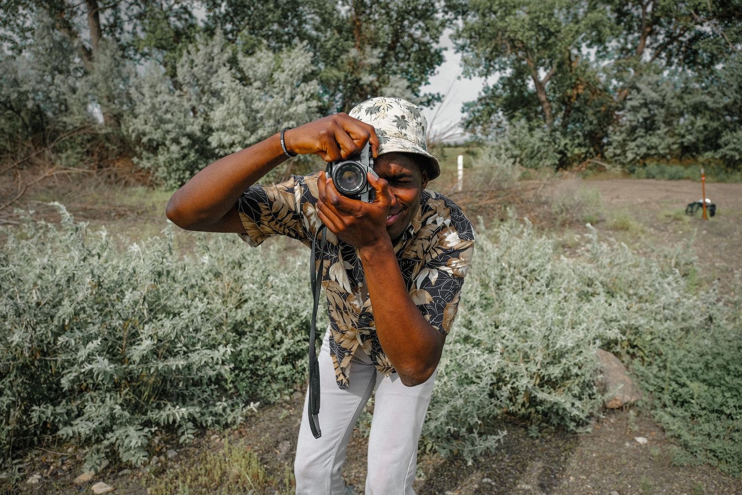 A photographer in camouflage gear takes a photo outdoors with a professional camera on a cloudy day.