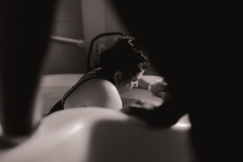 Black and white photo of a woman resting her head down during labor, captured in soft dramatic lighting.