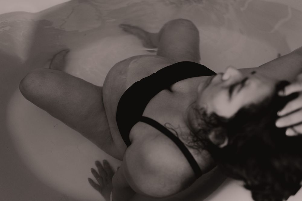 Pregnant woman relaxing in a bathtub, captured in a serene black and white maternity photography session.