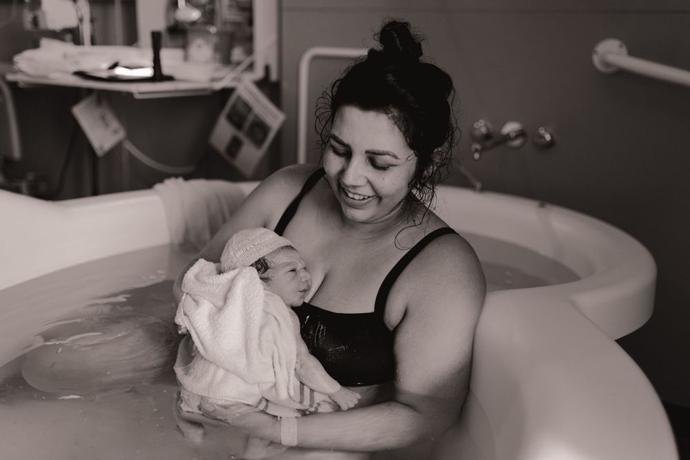 Black and white photo of a mother holding her newborn baby in a hospital birthing tub after water birth.
