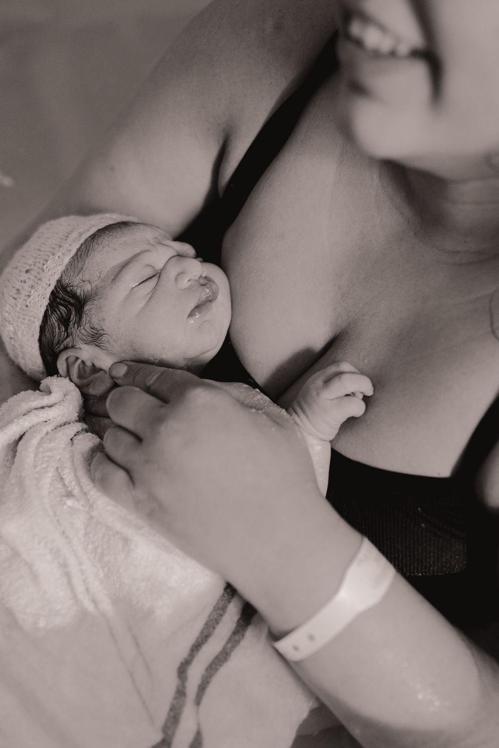 Black and white photo of a newborn baby in a knit hat being cradled by a mother after birth.