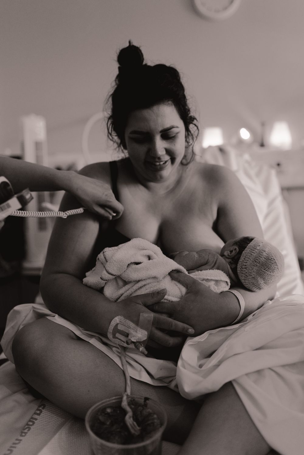 Black and white photo of a smiling new mother holding her newborn baby in a hospital bed after delivery.