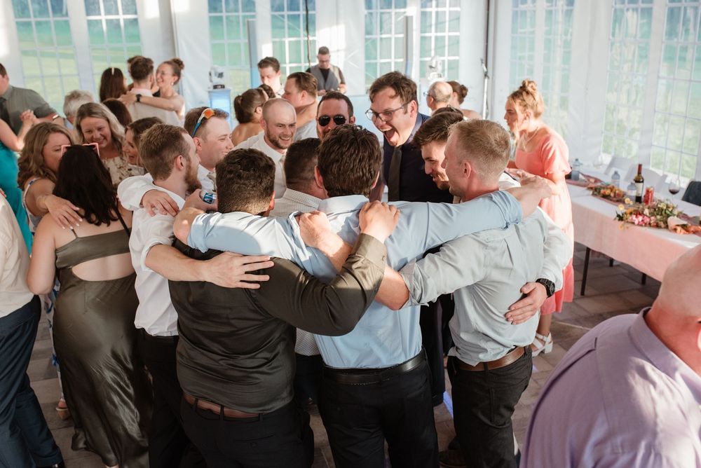 A large group huddles together in a circle at a celebration event in a bright indoor venue.