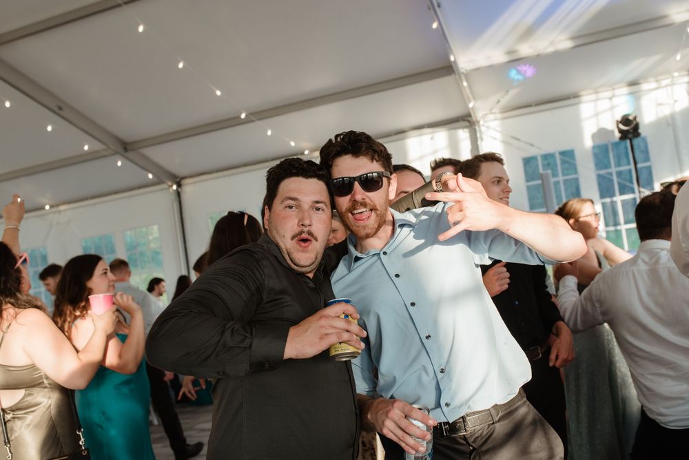 Party guests dancing and celebrating enthusiastically under a white tent at a lively wedding reception.
