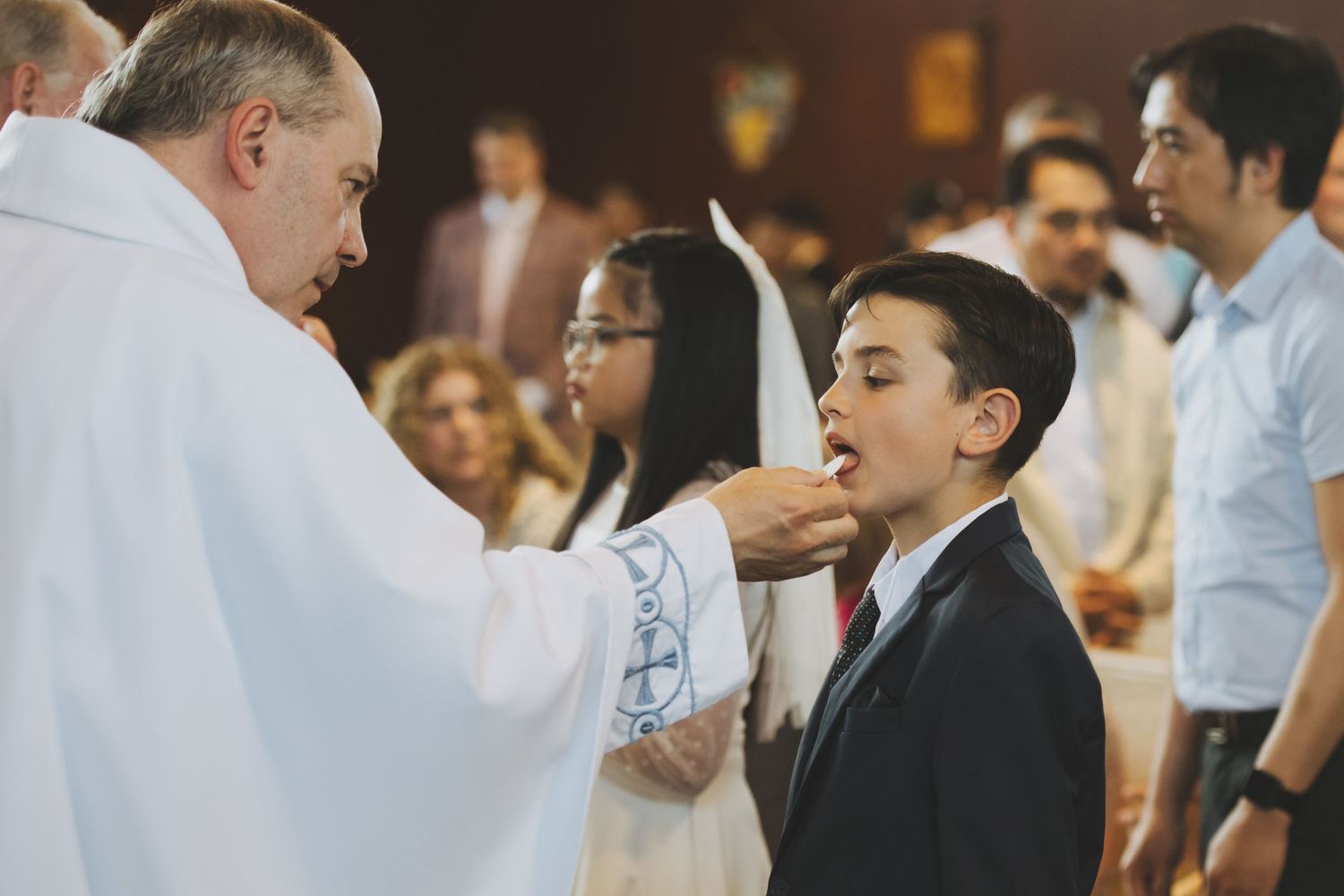 Young boy receives First Holy Communion from priest during traditional Catholic ceremony in church.