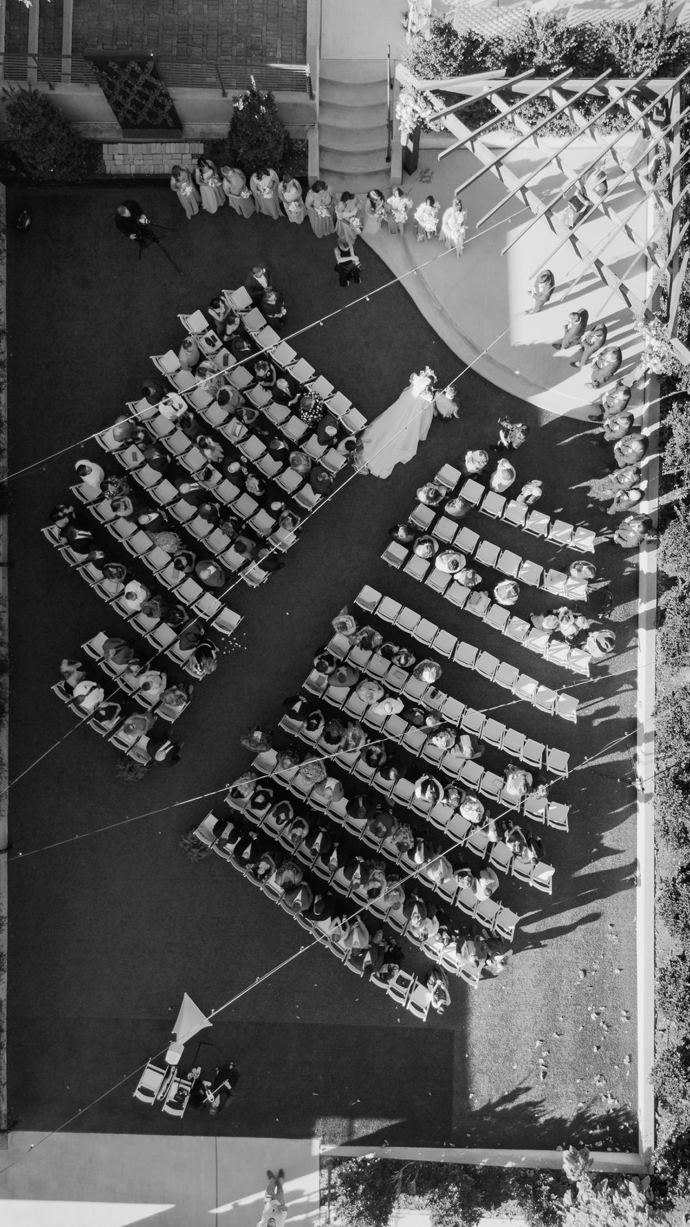Aerial black and white view of outdoor wedding ceremony with rows of seated guests and bridal party.