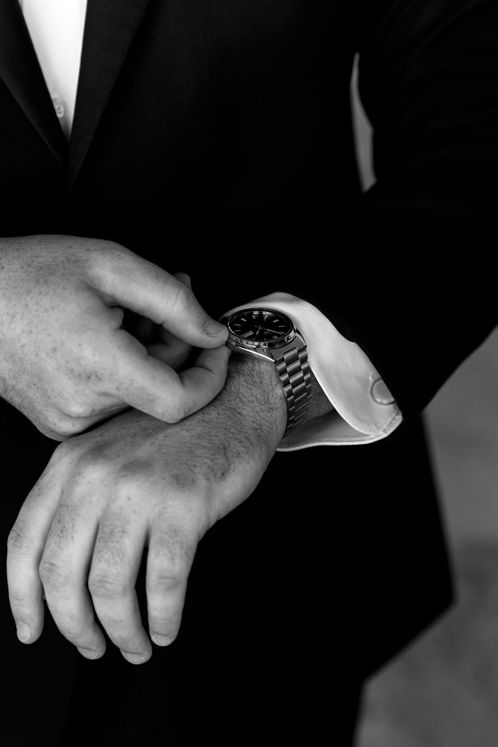 Close-up of groom adjusting his luxury watch while wearing a black suit and white dress shirt.
