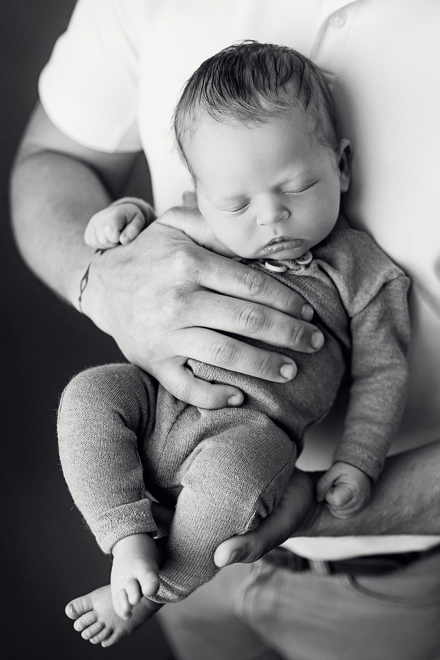 Father cradling sleeping newborn baby in black and white studio portrait