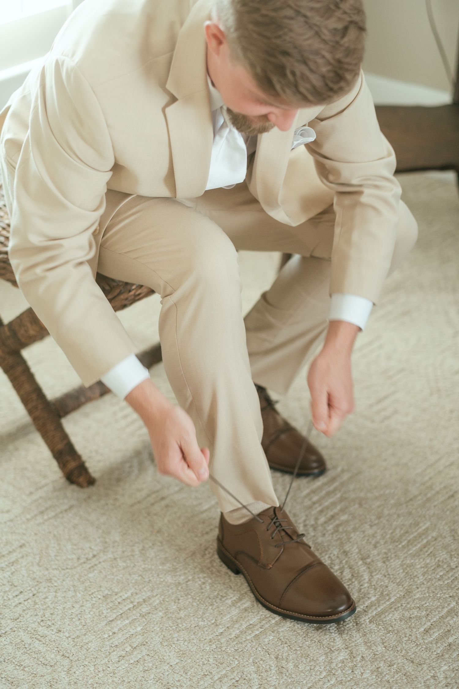 Person in beige suit adjusting brown dress shoes while getting ready.
