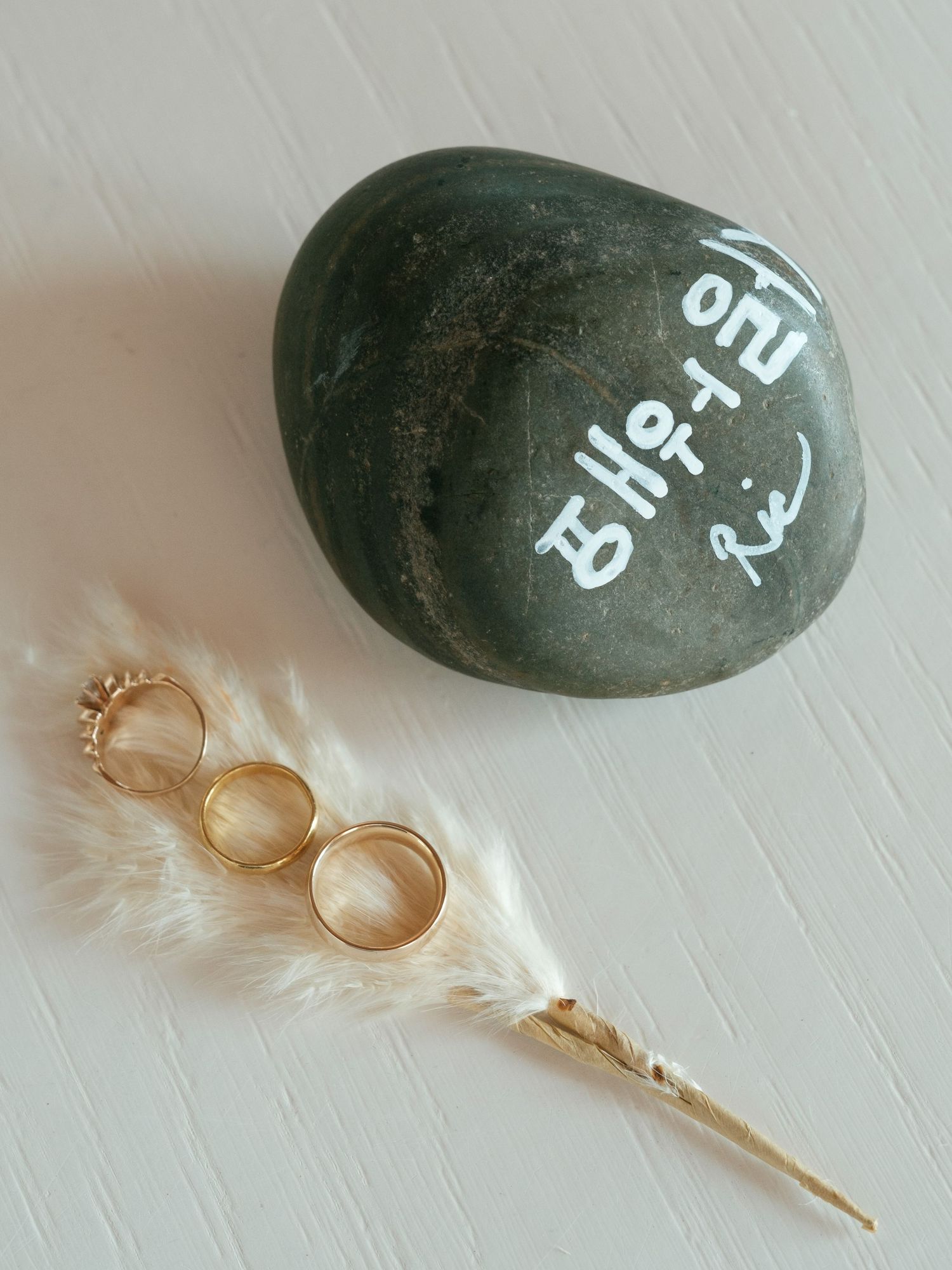 Wedding rings displayed on a white feather next to a green stone with writing on it.