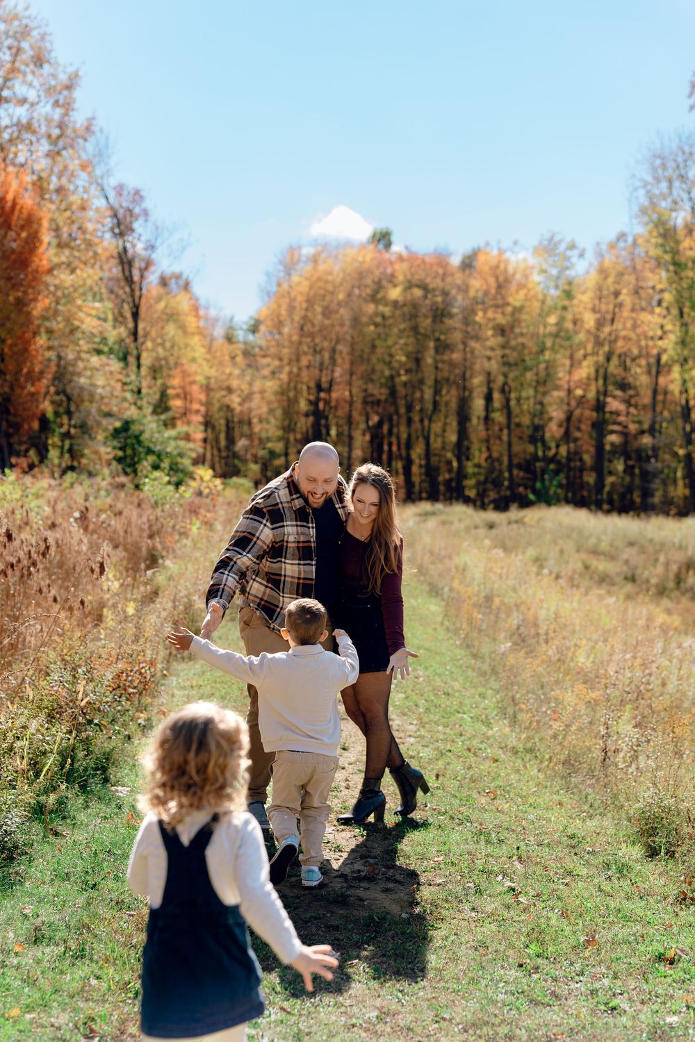 Family photos, enjoying a playful moment together in a scenic fall meadow with colorful foliage at Redemption Chapel Trail in Stow, Ohio.