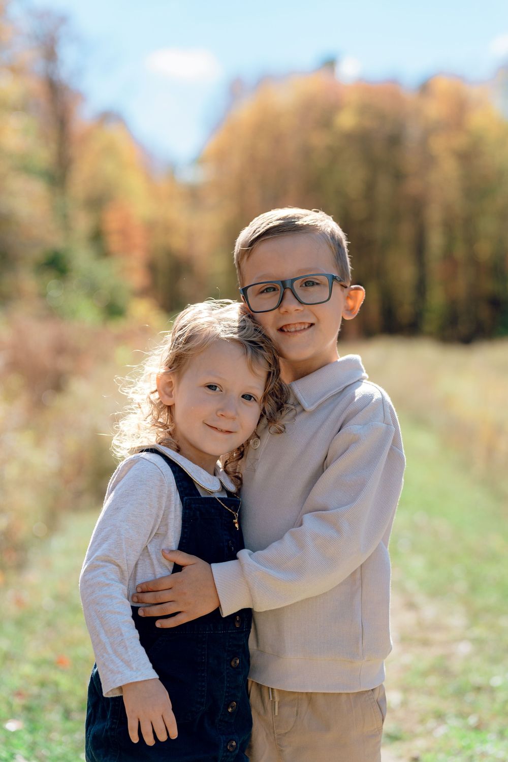 Two children share a sweet embrace in an autumn field with golden trees in the background in Stow, Ohio Redemption Chapel Trail.