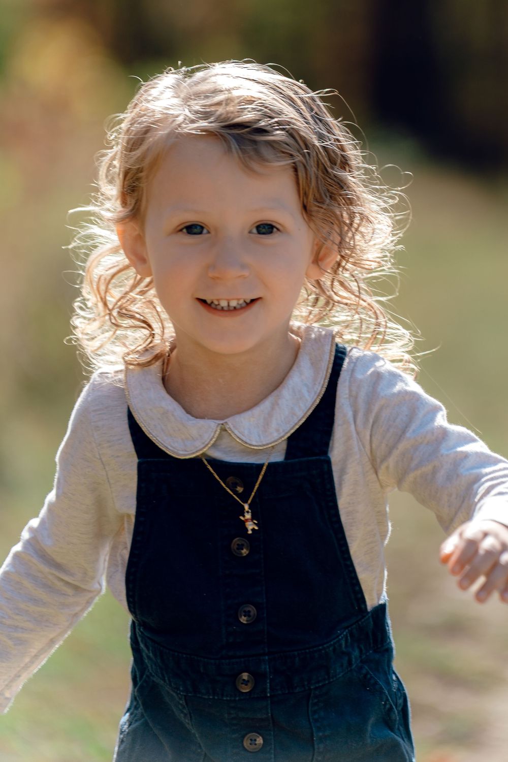 A toddler in a navy jumper dress smiles and plays outdoors at Redemption Chapel Trail in Stow, OH for Fall Family Photo Session