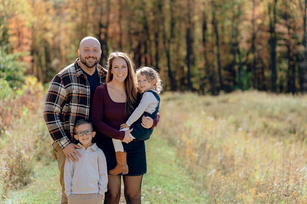 A family stands together in a grassy field during autumn with colorful fall foliage at Redemption Chapel in Stow, OH for family photos