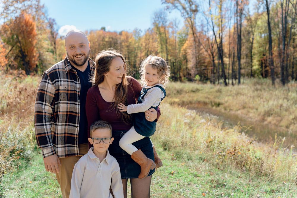 A family enjoys a playful moment together in an autumn field with colorful fall foliage in Stow, OH, Redemption Chapel Trail for Family Pics