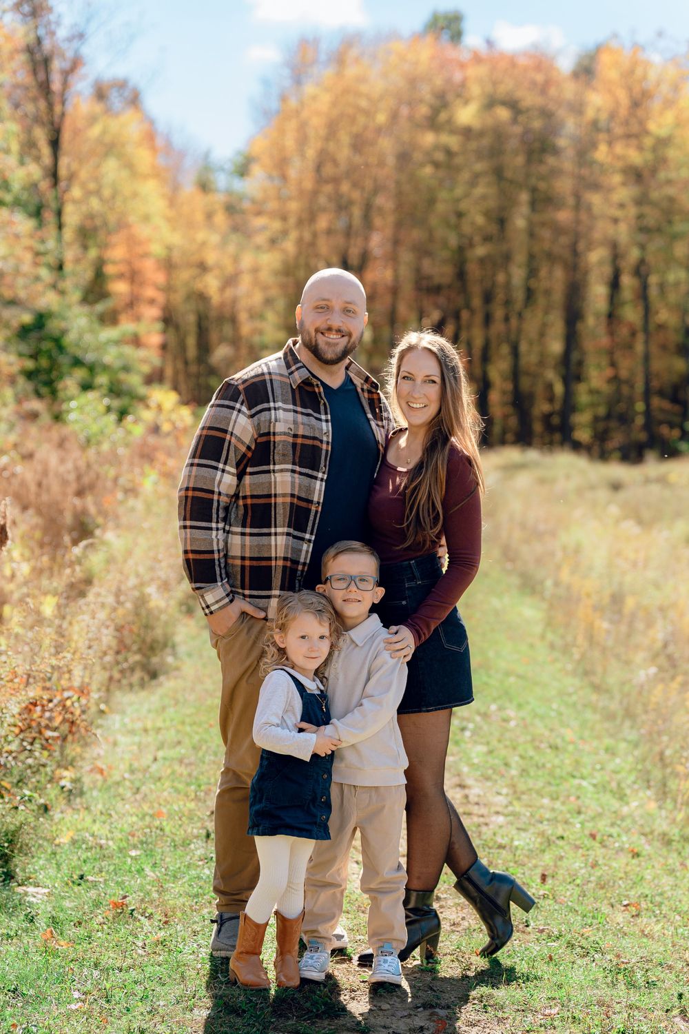 A family poses together in a field during autumn with golden trees in the background at Redemption Chapel in Stow, Ohio for Fall Family Pic