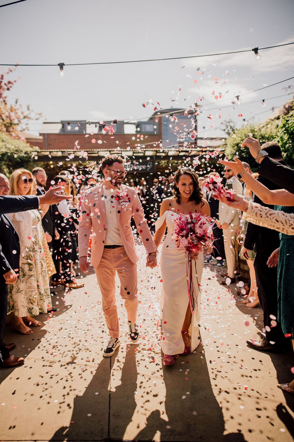 Wedding celebration with guests throwing confetti in sunlight creating joyful silhouettes during outdoor ceremony.