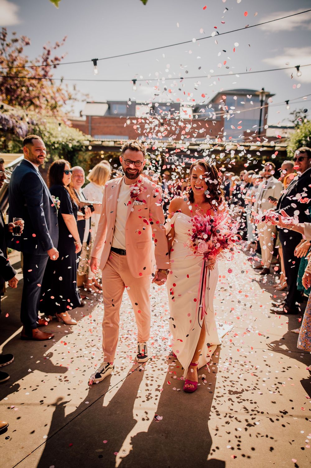 A wedding celebration sequence showing couples walking through a shower of pink and white confetti during an outdoor reception.