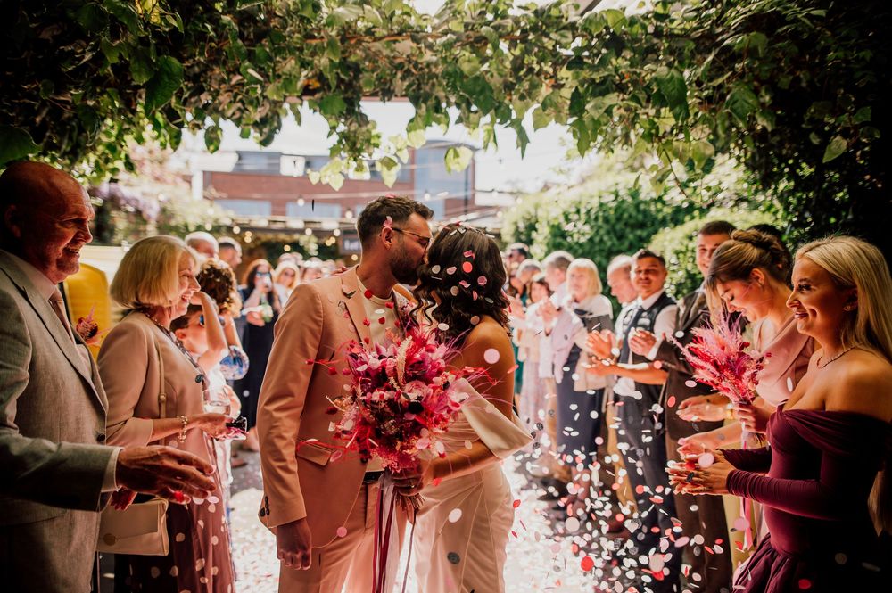 Wedding guests shower the happy couple with pink confetti during an outdoor summer celebration.