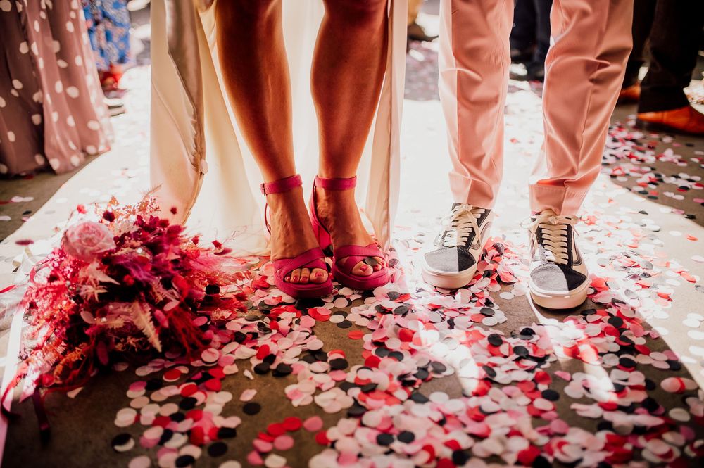 Feet of wedding guests dancing on floor covered with scattered red and pink rose petals during celebration.