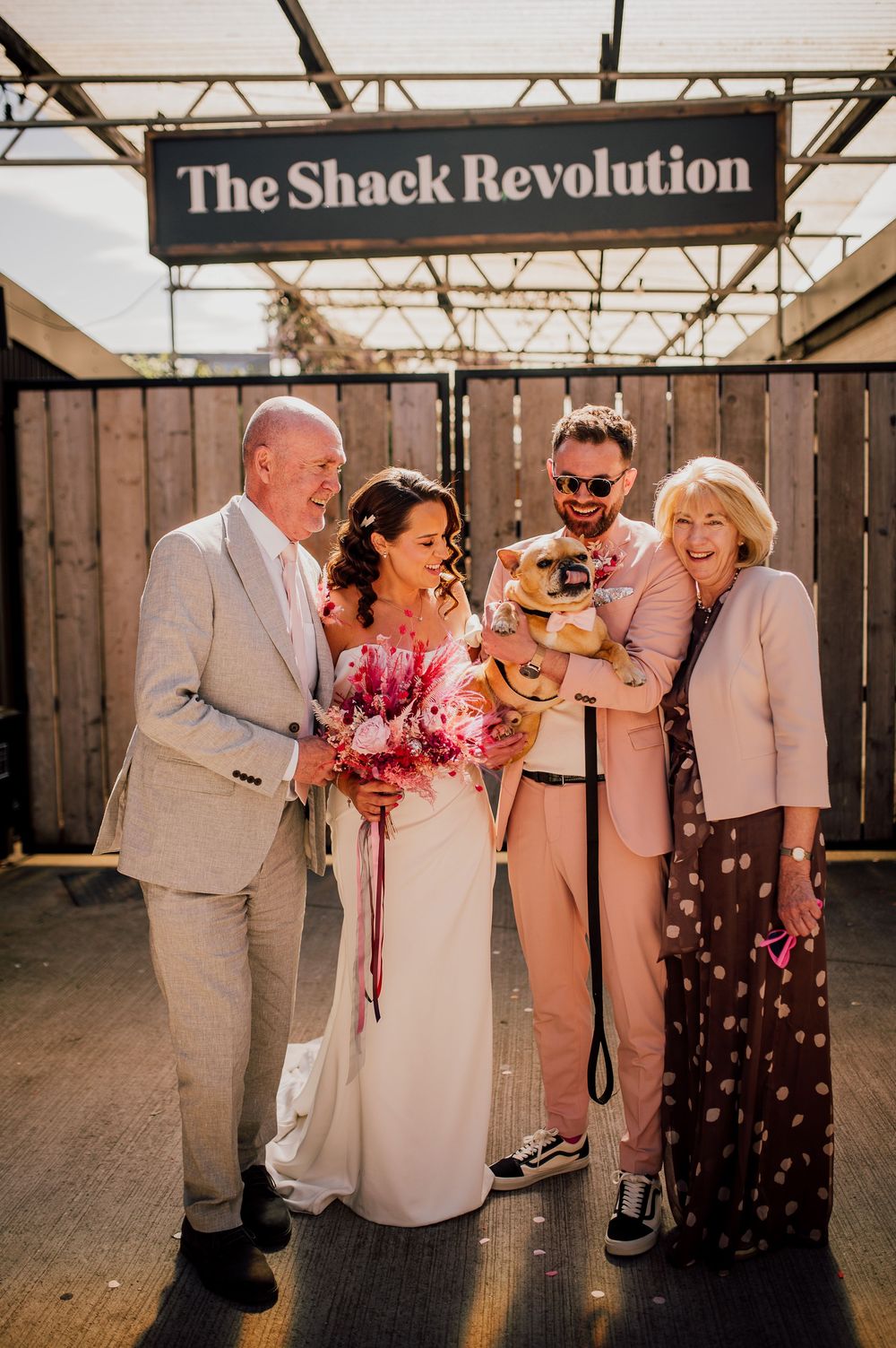 A group of wedding guests laughing and celebrating together in a rustic wooden venue with natural lighting.