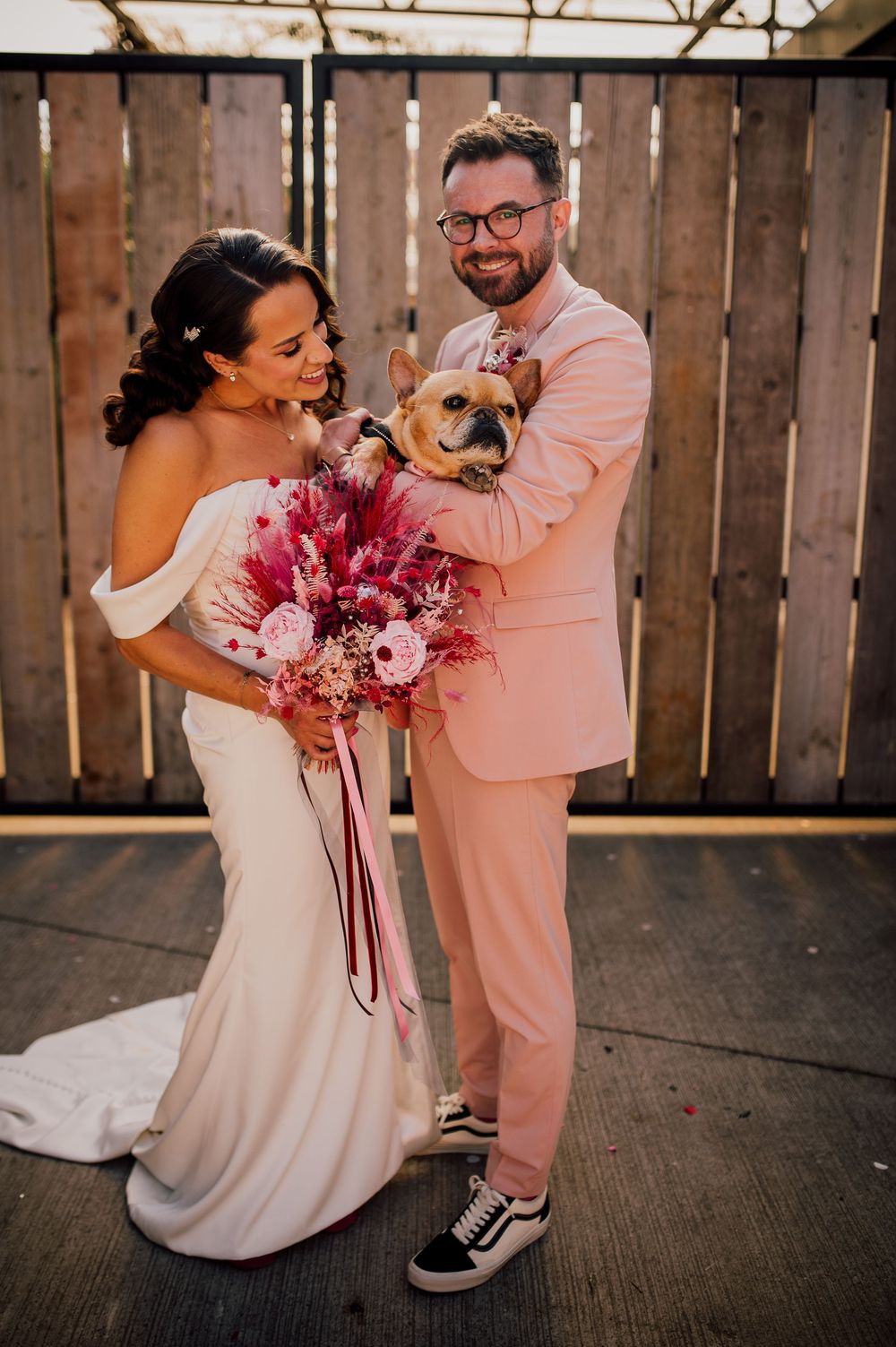 Newlywed couple dancing and twirling in a rustic barn venue with pink floral bouquet and casual wedding attire.