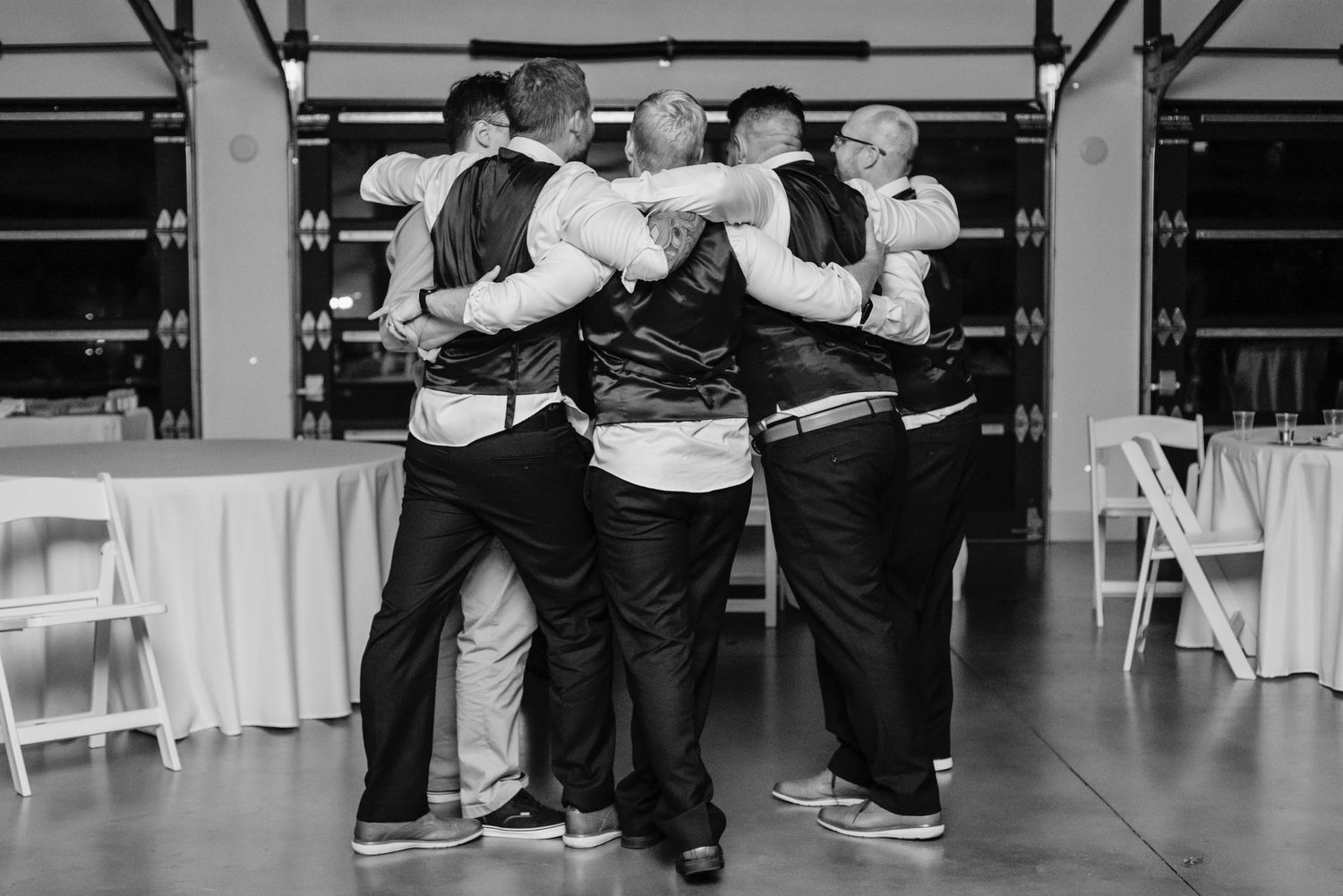A group of people wearing matching vests and dark pants huddle together in a circle at an indoor event venue.
