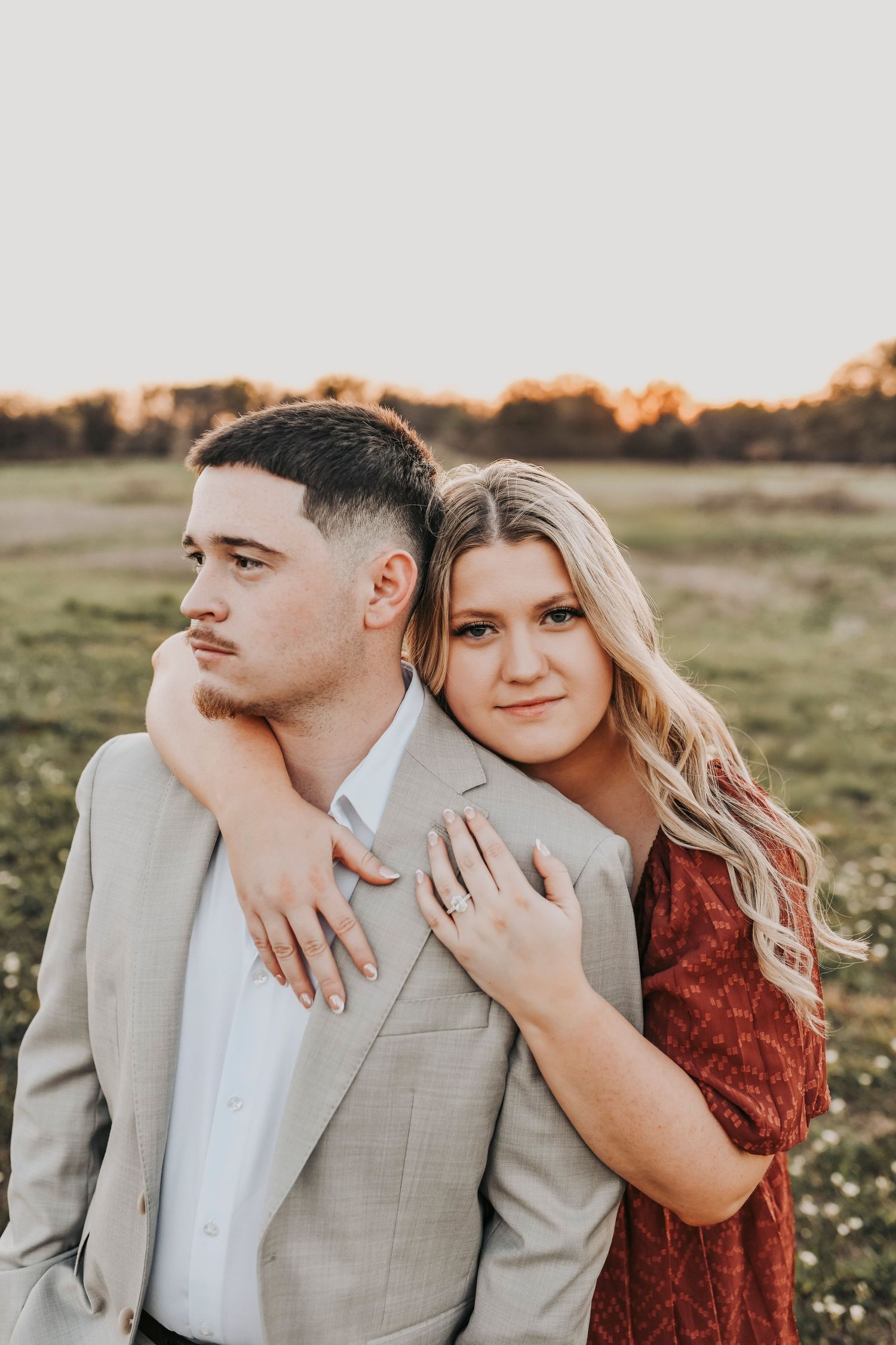 Engaged couple walking hand in hand through a scenic Texas field at sunset.
