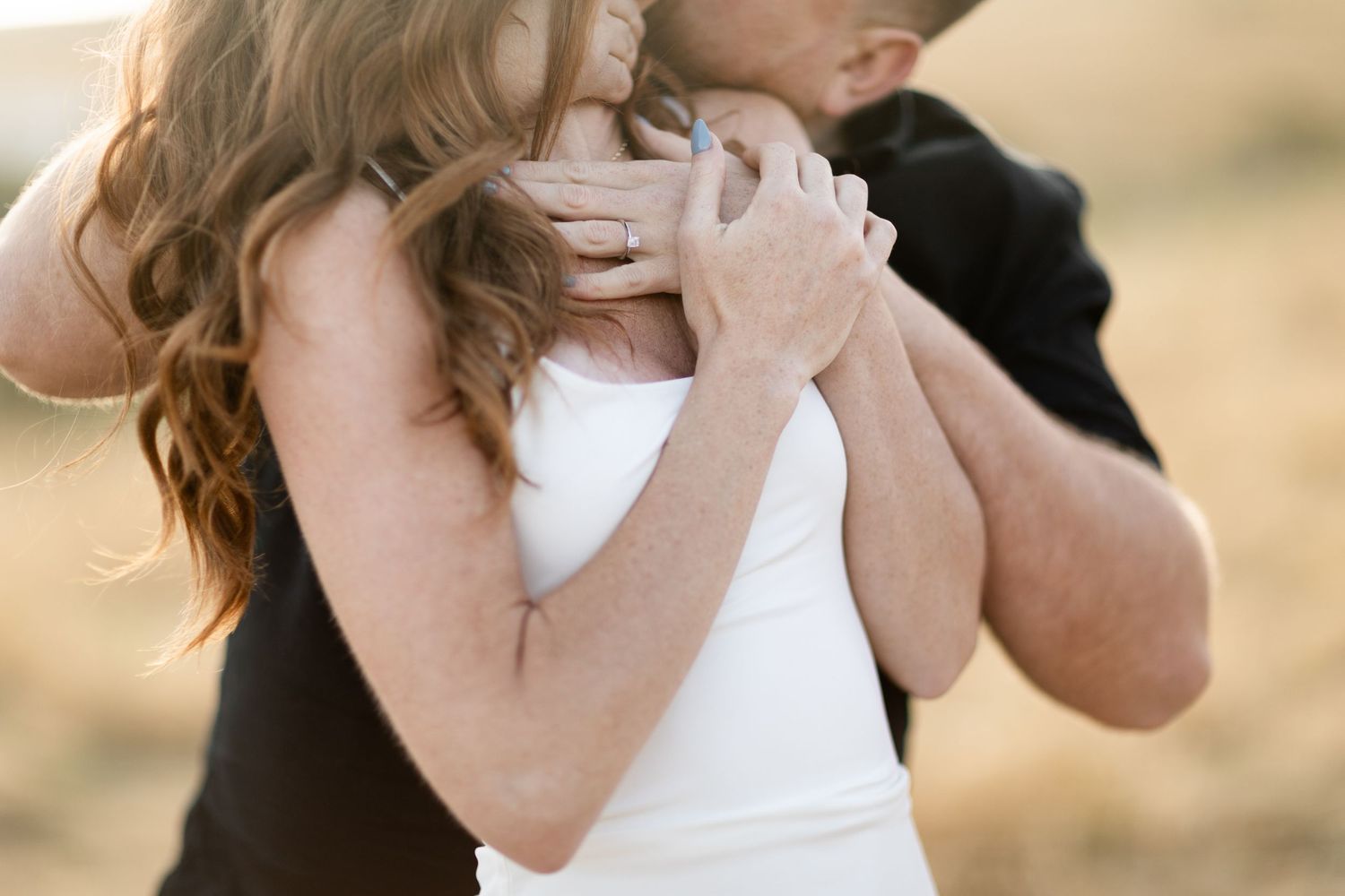A couple in formal wedding attire embraces and kisses outdoors during their special day.