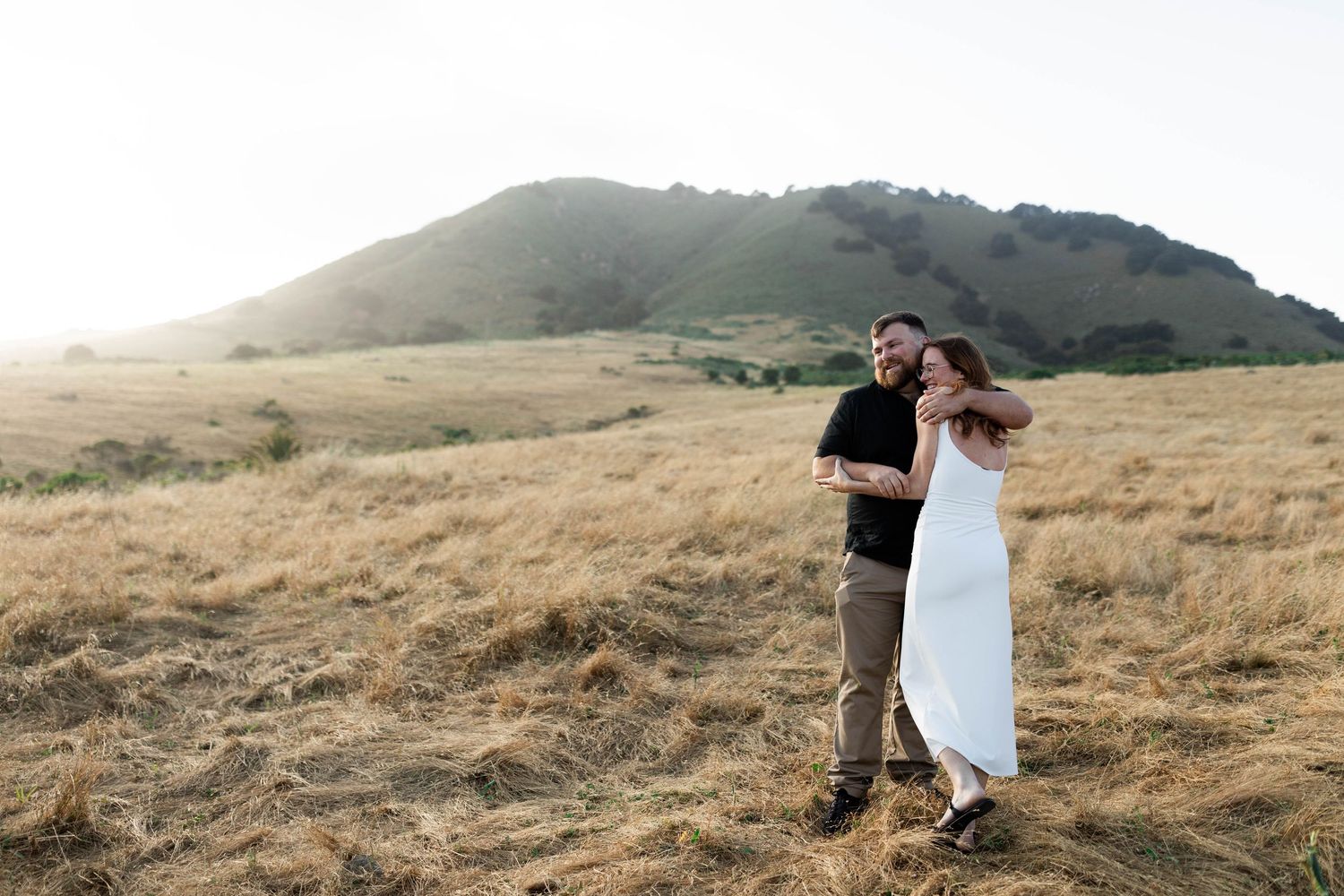 A couple walks hand in hand through golden rolling hills during sunset creating a romantic silhouette.