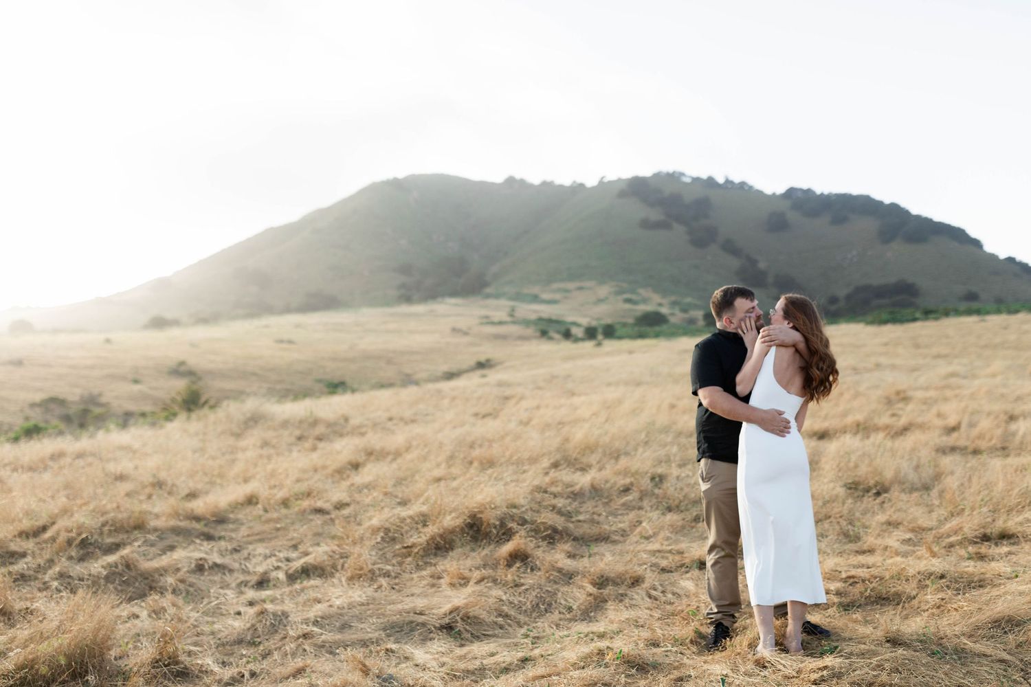 A couple embraces in a romantic moment on a golden hillside during sunset in California.