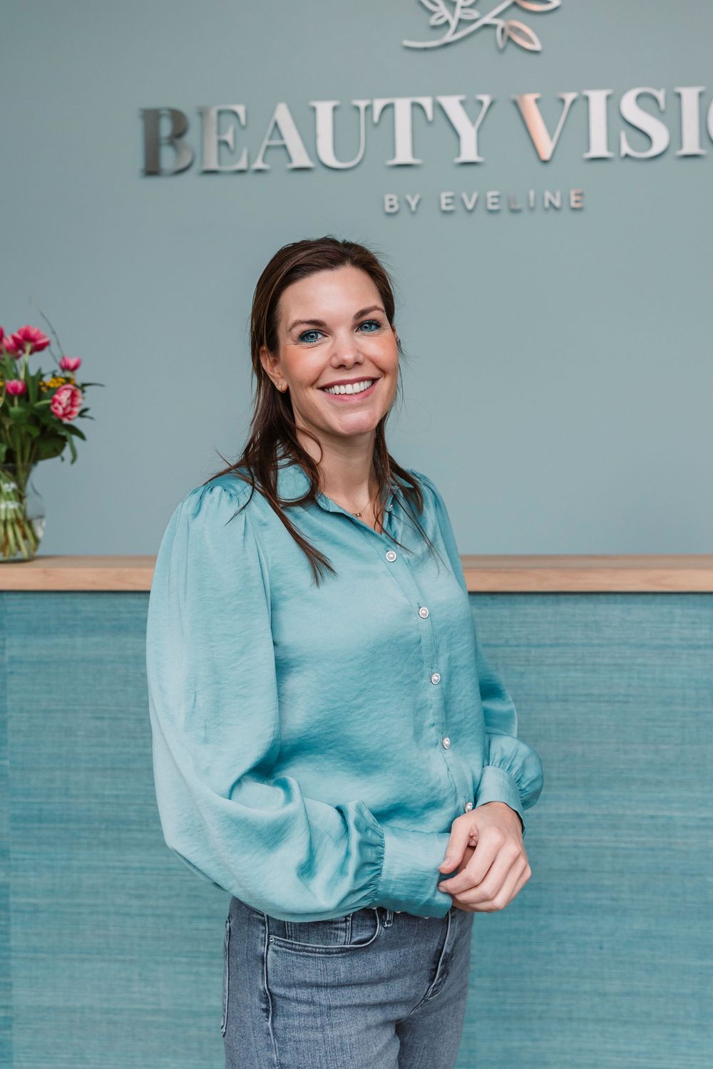 Staff member in teal blouse standing in front of Beauty Vision branded wall.