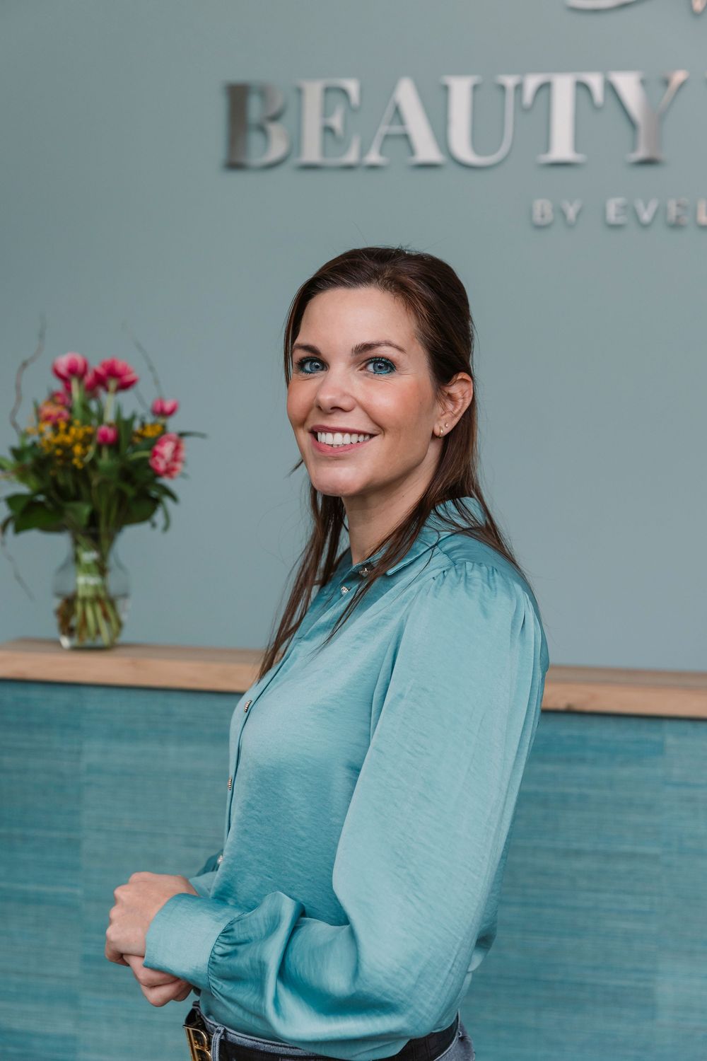 Professional posing in front of Beauty Vision logo wall with floral decor.
