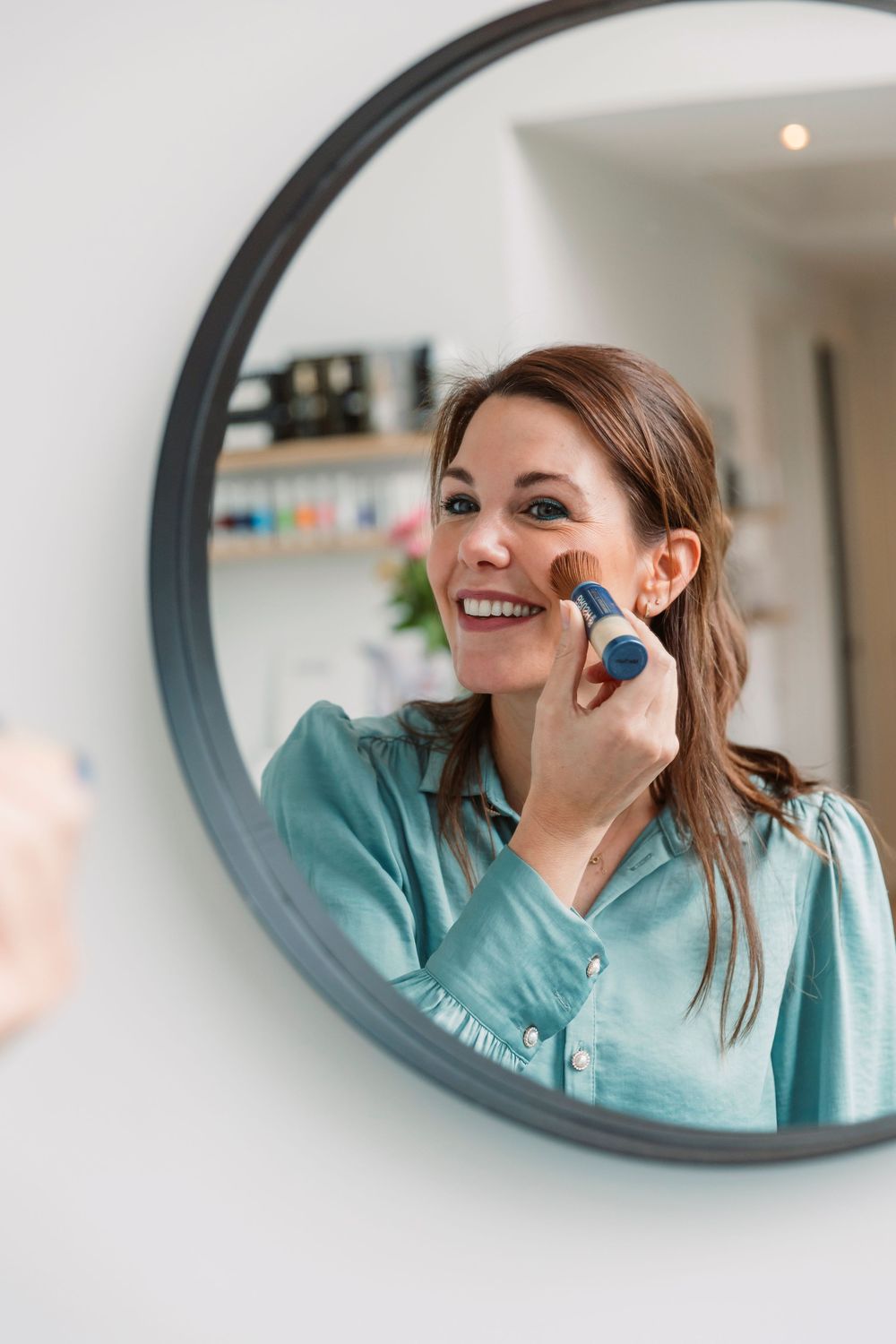 Reflection in round mirror shows professional applying skincare product.