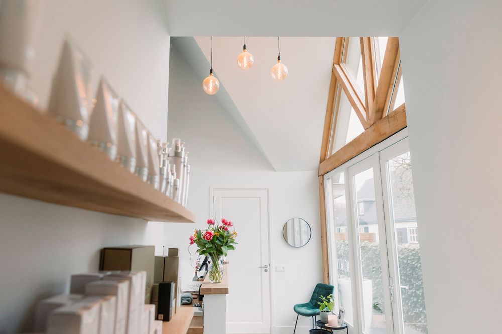 High-ceiling salon interior with pendant lights and wooden floating shelves.
