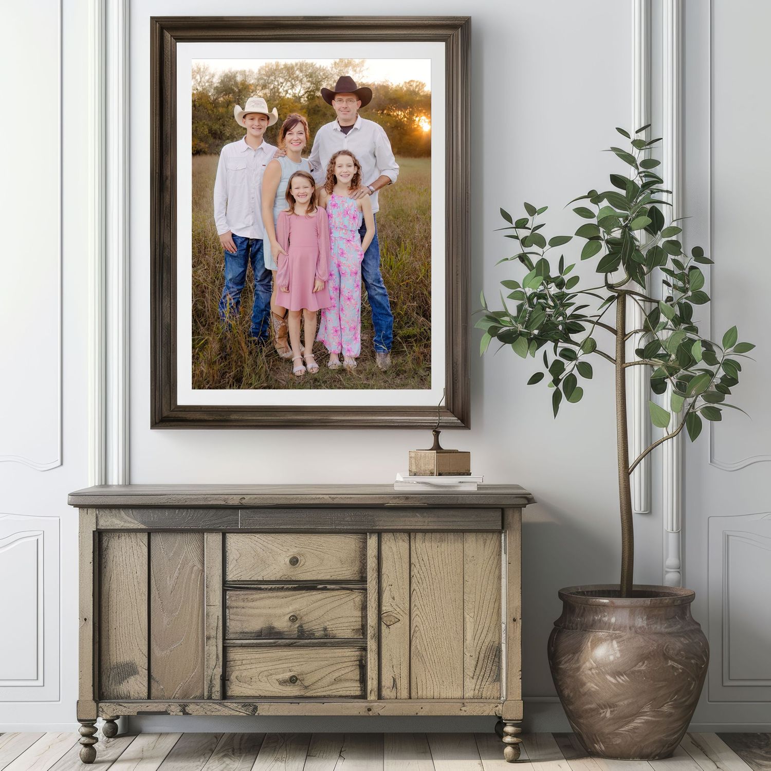 Framed family portraits displayed on a white wall with decorative plants and rustic wooden furniture beneath them.