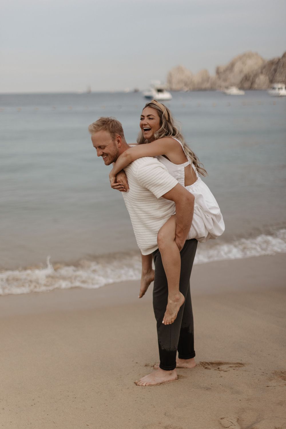 A playful couple embraces and laughs together on a foggy beach during a romantic moment.
