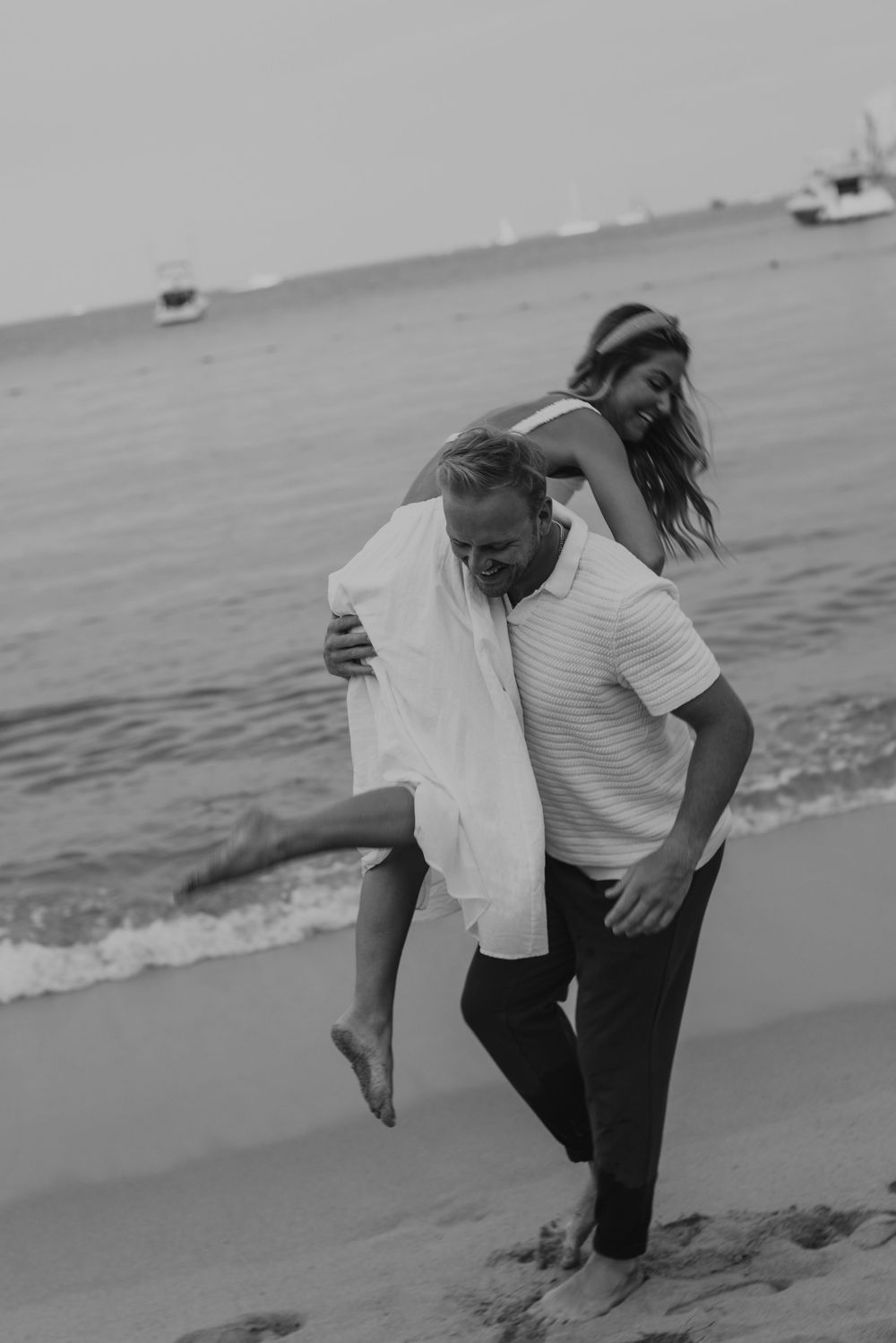 A playful black and white photo of a couple having fun together on a beach near the water.
