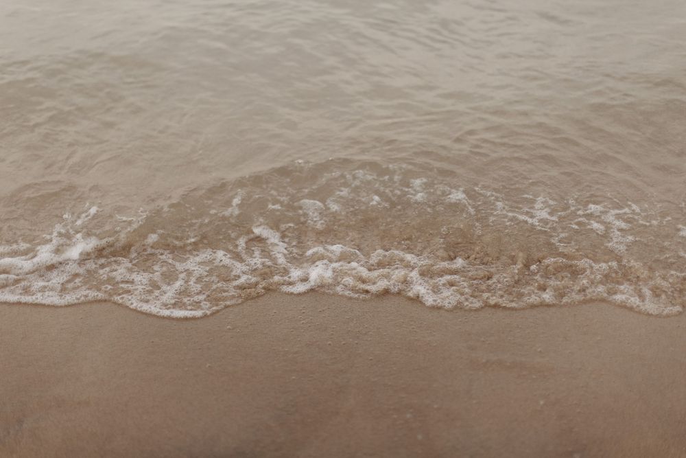 Gentle ocean waves washing up on sandy beach shore in a minimalist composition.