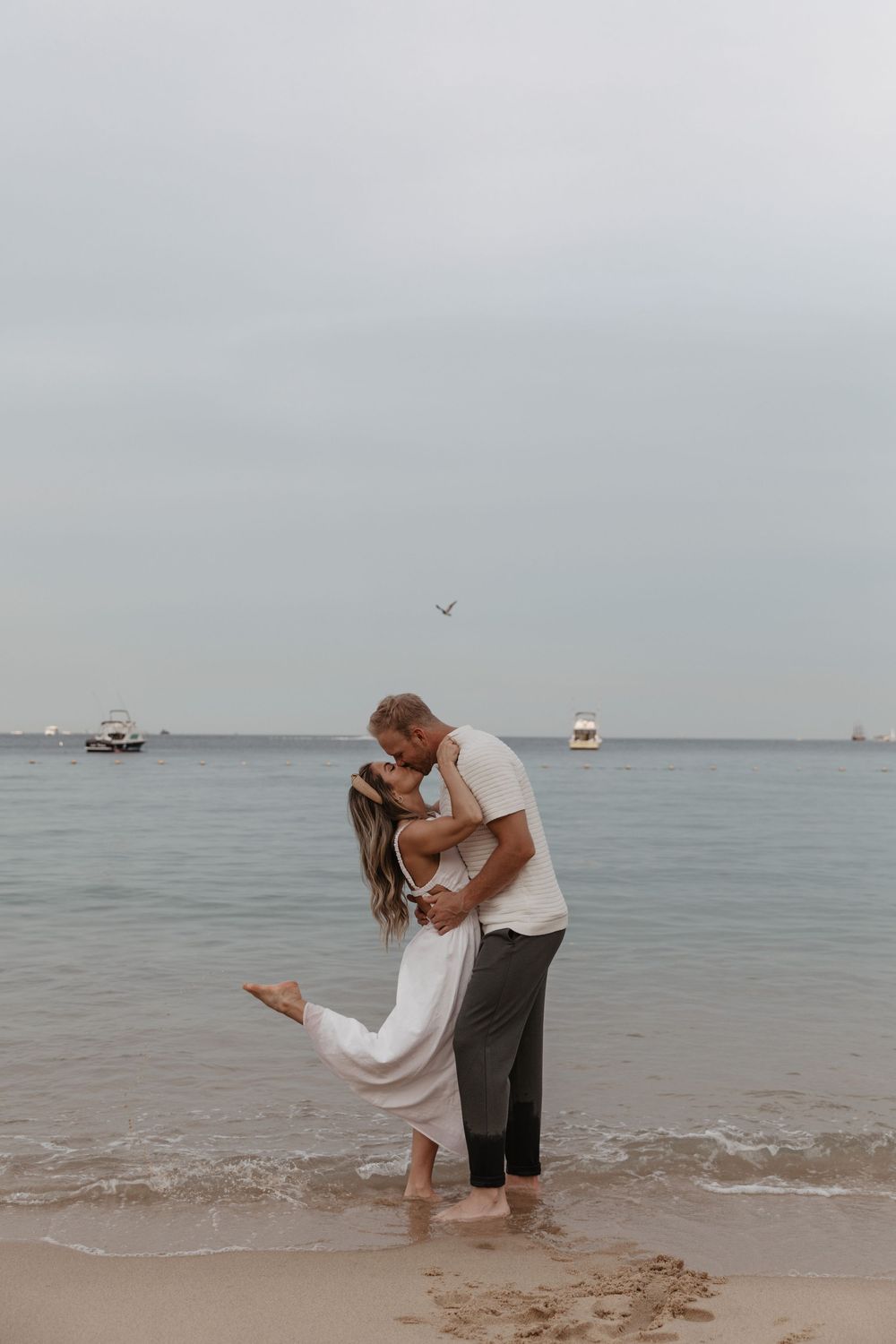 A couple shares a romantic moment at the beach's edge as waves gently lap at their feet.