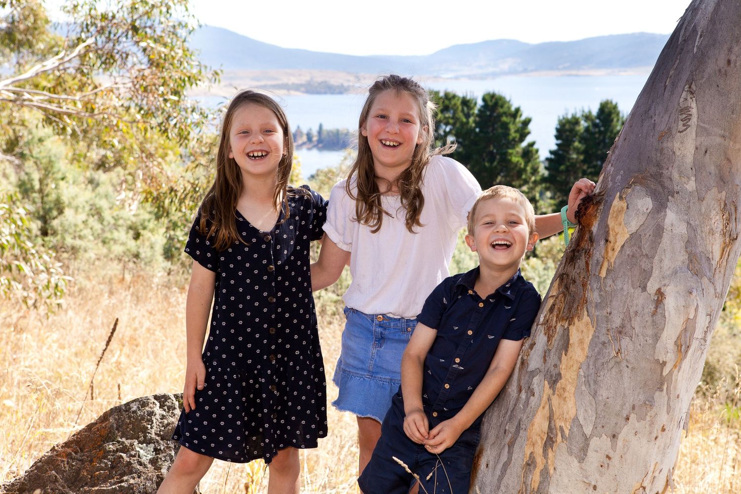 Children enjoy a sunny autumn day outdoors near a rocky hillside with golden foliage in the background.