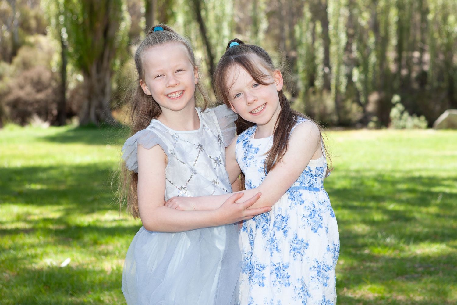 Children in coordinating blue and white outfits gather for outdoor portraits in sunlit garden setting.